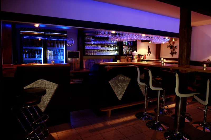 Bar mit Hockern, Kühlschränken und hängenden Gläsern.