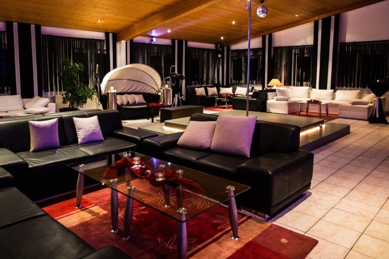 Lounge mit schwarzen Sofas, einer Bühne und einer Tanzstange.