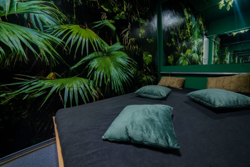Bett mit grünen Kissen vor einer Wand mit großen Blättern.